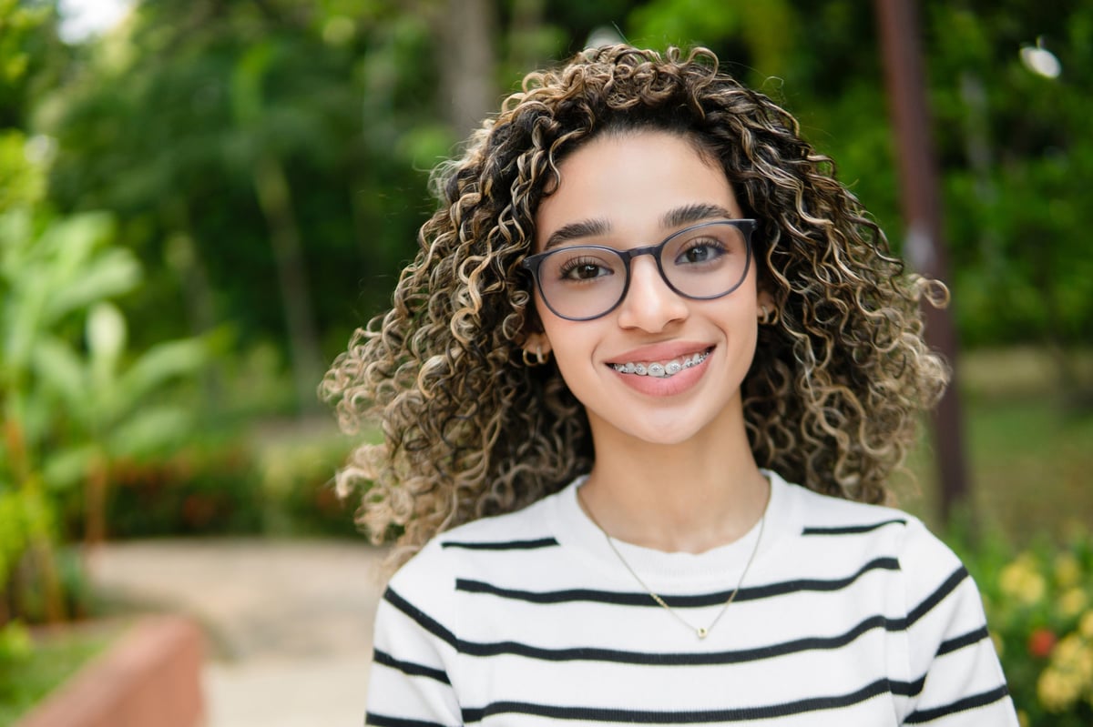 Joven estudiante con brackets y lentes sonriendo en campus universitario, reflejando diversidad y educación