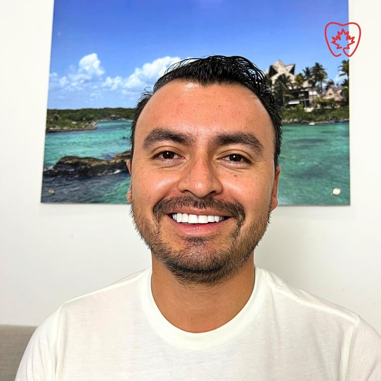 Smiling man with dark hair and beard wearing white t-shirt, tropical beach photo on wall behind him