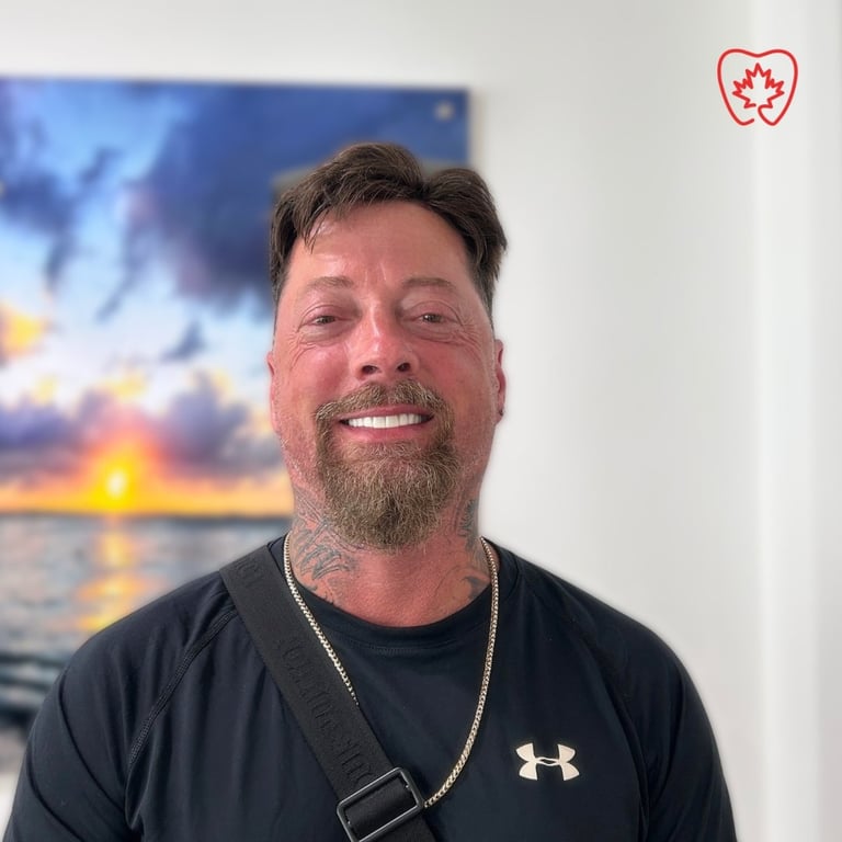 Man with beard wearing black Under Armour shirt and chain necklace, smiling at camera with sunset photo in background